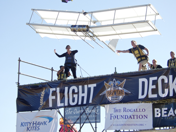Outer Banks Visitors Bureau launching their Wright Flyer. The glider seemed to be in flight longer than any other, although it did not qualify by distance. Standing on the edge to the left is Allison Wyant. Pushing the tail is Aaron Tuell, Amy Wood to his right and Bruce Weaver of Kitty Hawk Kites.
