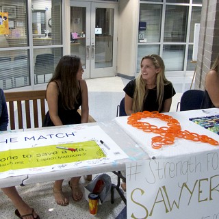 Helping to pay for treatment and research. First Flight High School students man Sawyer's support table.