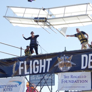 Outer Banks Visitors Bureau launching their Wright Flyer. The glider seemed to be in flight longer than any other, although it did not qualify by distance. Standing on the edge to the left is Allison Wyant. Pushing the tail is Aaron Tuell, Amy Wood to his right and Bruce Weaver of Kitty Hawk Kites.